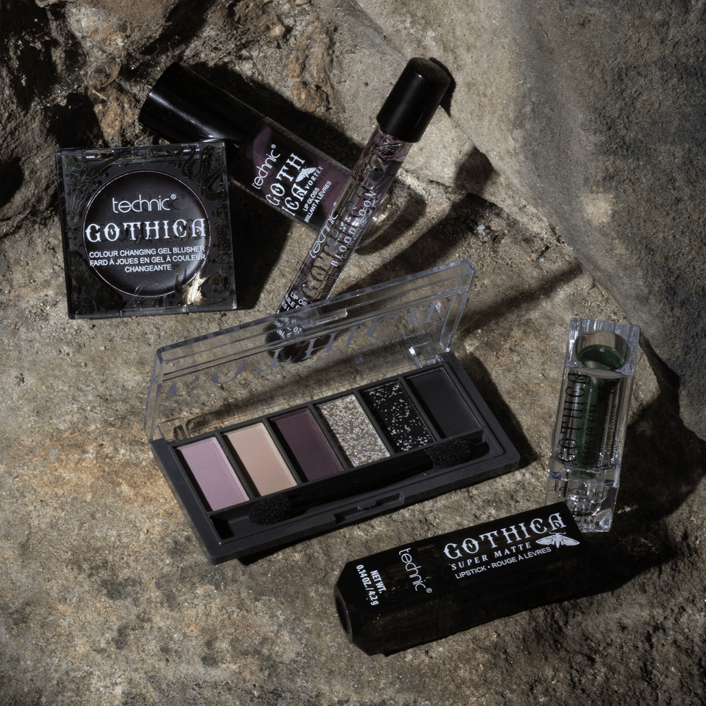 Some other gothica products including lip oils, lipsticks, blusher and eyeshadow palette. This is all on a stone wall background.