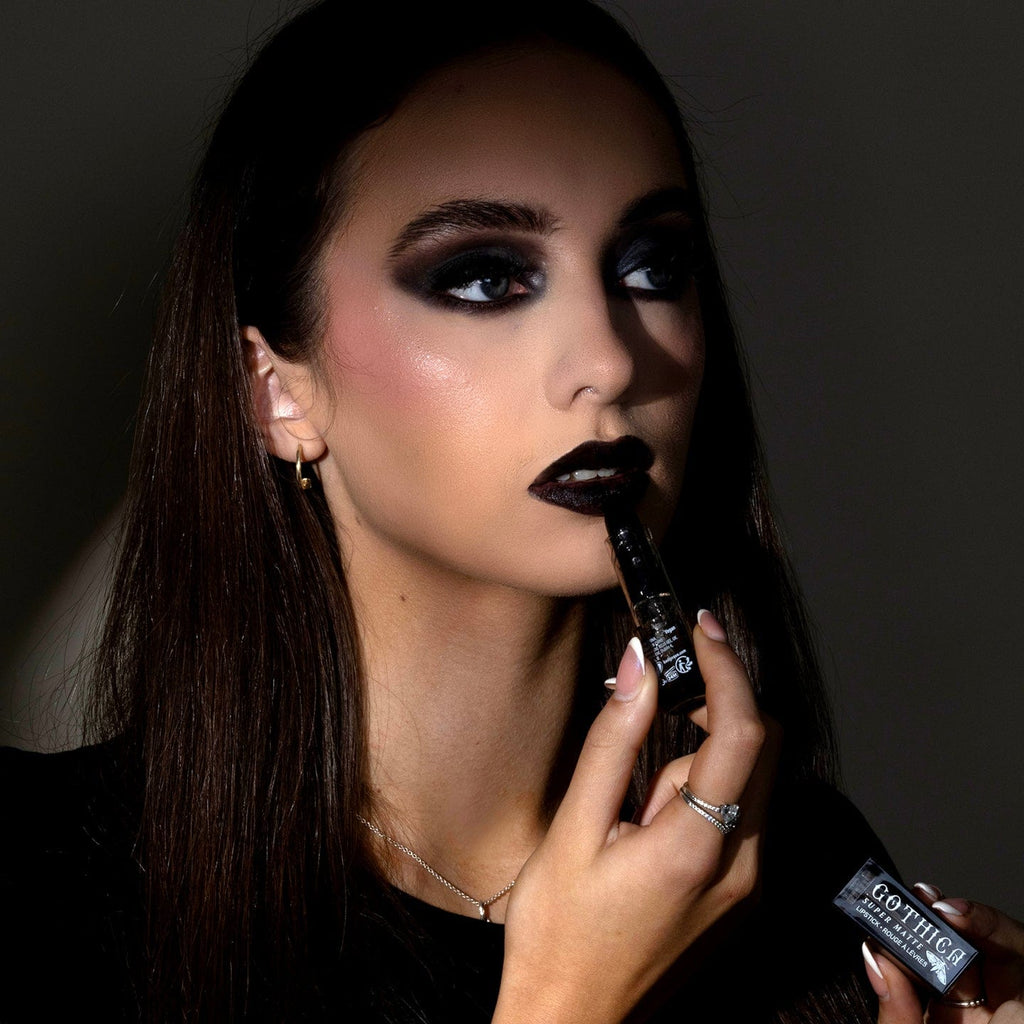 Woman applying black lipstick with a dark background