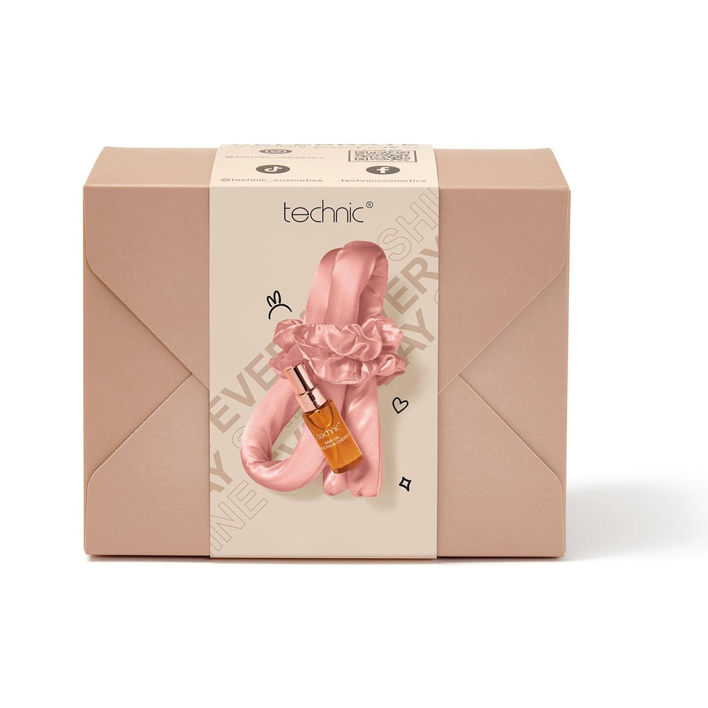 The heatless hair curler giftset on a white background. The giftset is a beige box with a seal around it to show contents. Inside the giftset is a pink heatless curler, matching pair of pink scrunchies and a bottle of hair oil.