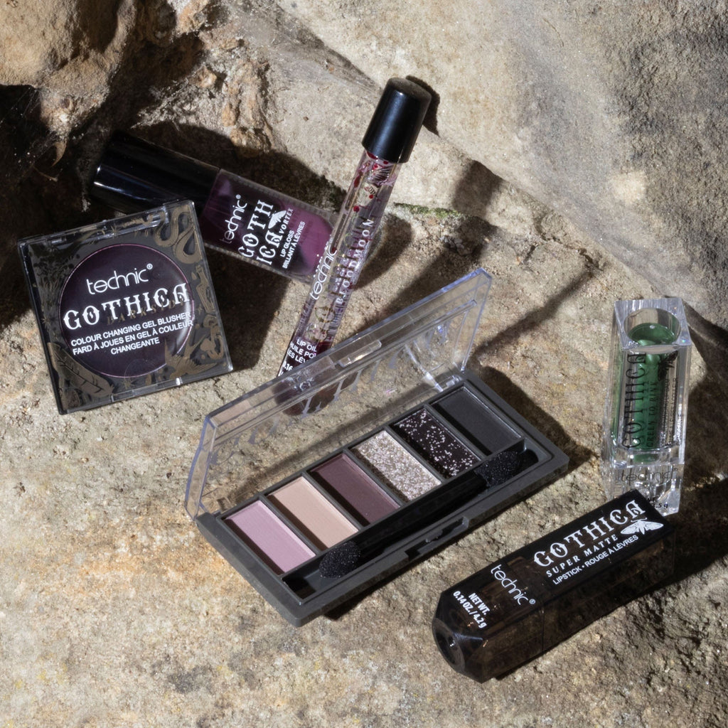 Some other gothica products including lip oils, lipsticks, blusher and eyeshadow palette. This is all on a stone wall background.