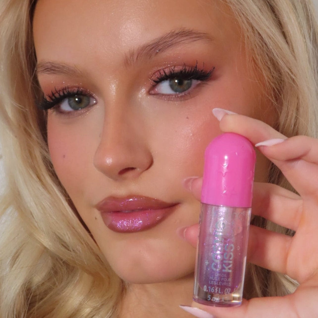 Woman wearing and holding a pink glitter lip gloss with a blurred background