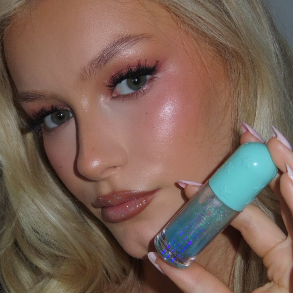 Woman holding a turquoise shimmer lip gloss with a blurred background