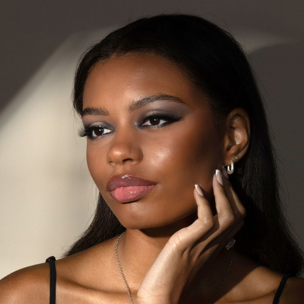 Woman with makeup posing with hand by face against a neutral background